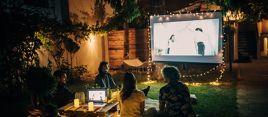 Four friends in small yard with projector, laptop, string lights, watching movie